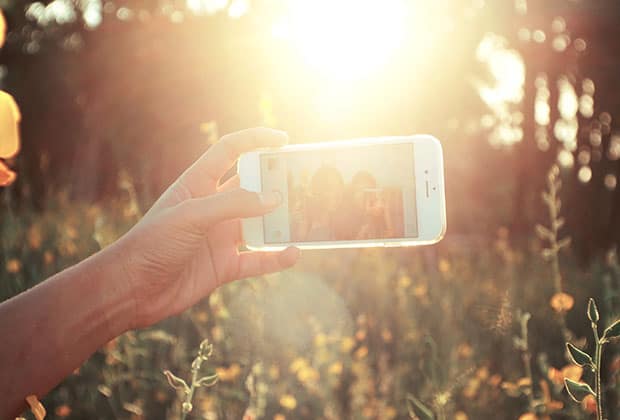 Hand holding out iphone for selfie in the sunshine