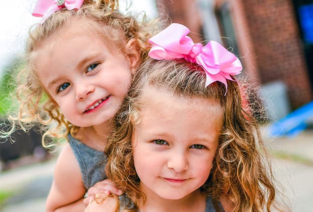 Curly-haired sisters in matching bows play